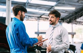 Caucasian automotive maintenance mechanic young man explain car condition to male customer in garage at auto repair shop, technician writing document on vehicle checklist, after service concept